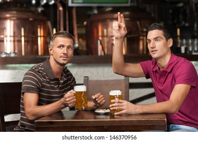 One more beer please! Two friends drinking beer at the pub while one of them asking a waiter.