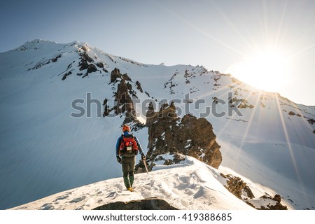 One mountaineer climbs rocky, snowy mountain at dawn.