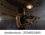 One music player with classic wooden violin. Soloist musician playing sounds of acoustic melody by bow. Magnificent work of pretty woman as orchestral violinist indoors at large room of great theater