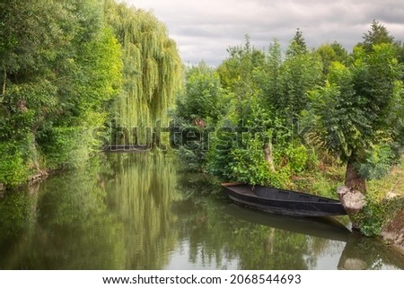 One of the navigable canals of the picturesque marshlands of the Regional Natural Park of the Marais Poitevin, with rowboats and weeping willows on the water