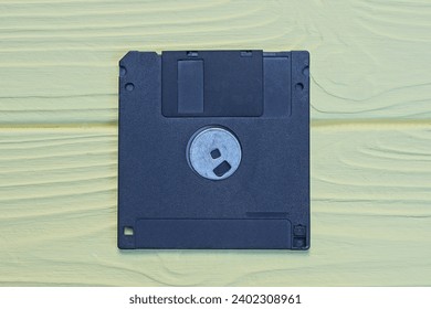 one old black square plastic computer floppy disk lies on a yellow wooden table