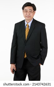 One Old Businessman In Formal Black Suit Yellow Tie. Standing Look At Camera One Hand Put In Pant Pocket Other Hand Holding Mobile Phone. Studio Shoot With White Background