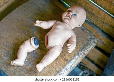 One Old Dirty Plastic Doll Toy With A Broken Leg Lies On A Brown Table