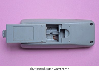 one old gray plastic remote control with open battery pack and cover on a pink table