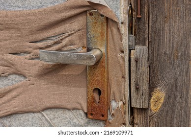 One Old Rusty Brown Metal Doorknob On A Tattered Fabric Door Outside