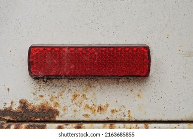 One Old Small Rectangular Red Plastic Turn Signal Reflector On White Car Metal In Brown Rust