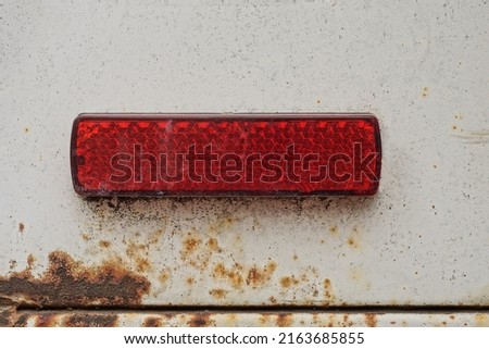 one old small rectangular red plastic turn signal reflector on white car metal in brown rust