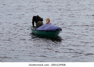 One old unmanageable loaded rowing boat on the water with a family of tourists, a man at the stern repairs a stalled outboard motor, an emergency incident with an immobilized boat on the water - Powered by Shutterstock