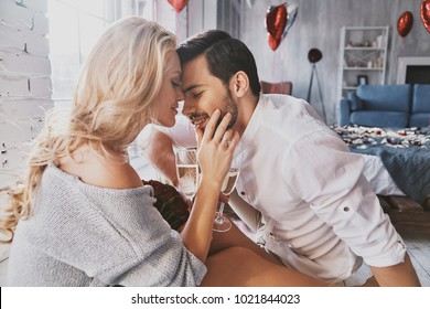 One and only. Beautiful young couple drinking champagne and smiling while sitting face to face in the bedroom - Shutterstock ID 1021844023