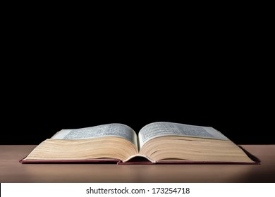 One Open Bible On Table In Black Background