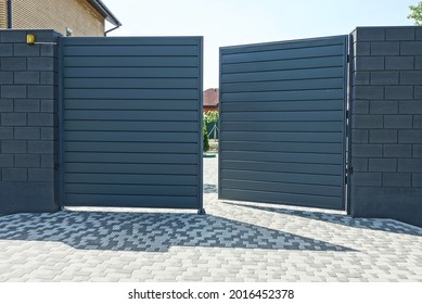 one open black metal gate and part of a brick wall of a fence on the street on a gray sidewalk - Shutterstock ID 2016452378