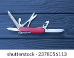 one open folding knive multitools with red handles with gray blades lies on a black wooden table