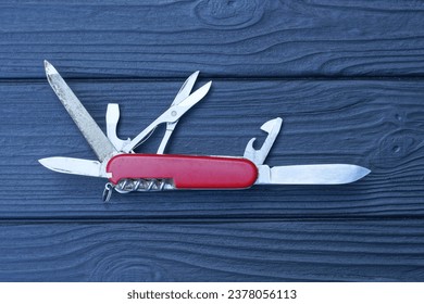 one open folding knive multitools with red handles with gray blades lies on a black wooden table