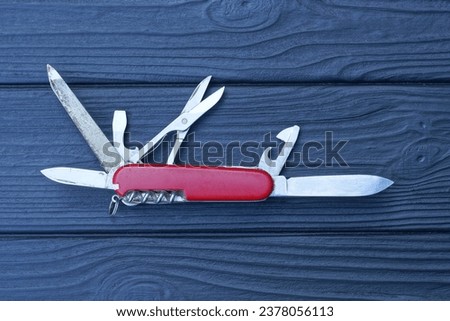 one open folding knive multitools with red handles with gray blades lies on a black wooden table