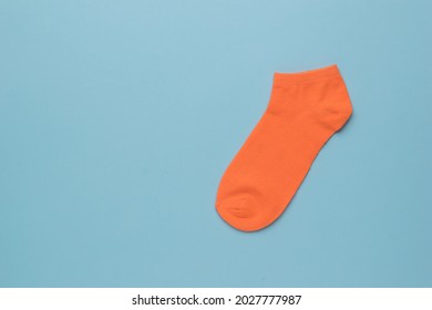 One Orange Sports Sock On A Blue Background. A Stylish Sports Accessory. Flat Lay.