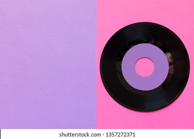 One outdated vinyl record on a three-ton paper background: pink and violet, pop culture. Top view. Minimalism, top view with copy space