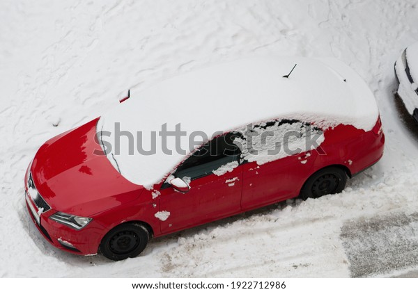 One parked car stand in a snowy parking lot and is\
covered with snow. A snowstorm struck. The cars and roads are under\
the snow.