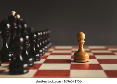 One pawn standing against set of black chess. Alone against many enemies, symbol of difficult fight or struggle, confidence concept