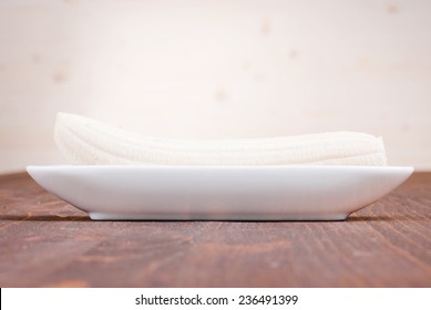 One Peeled Banana On A Plate On A Brown Table Side View