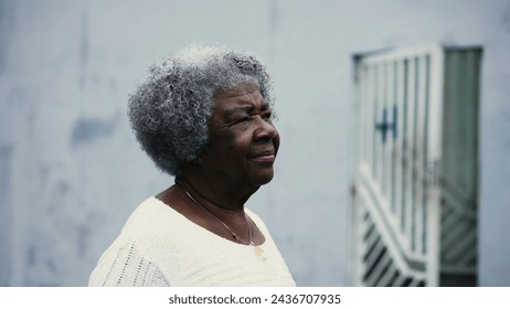 One pensive black senior woman strolling outdoors in city street with thoughtful gaze, close-up face tracking shot. Active African American elderly lady walking forward