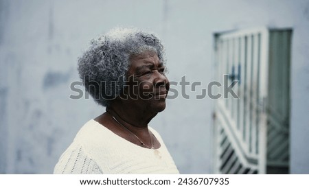 One pensive black senior woman strolling outdoors in city street with thoughtful gaze, close-up face tracking shot. Active African American elderly lady walking forward
