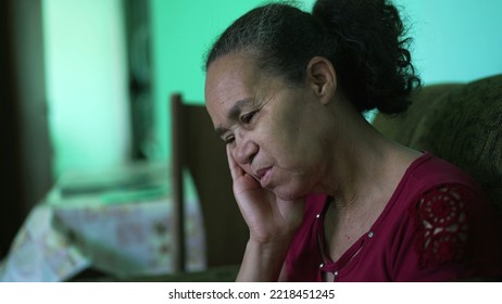 One Pensive Hispanic Older Woman Sitting At Couch. A Contemplative Worried Latin American Senior Person