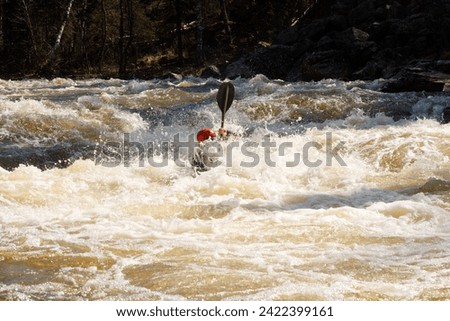 One person in red hat paddles river with sports