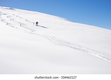 One person skiing downhills off piste on snowy slope in the italian Alps, with bright sunny day of winter season. Thick Powder snow with ski tracks.