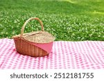 One picnic wicker basket with checkered napkin and blanket on green grass. Space for text