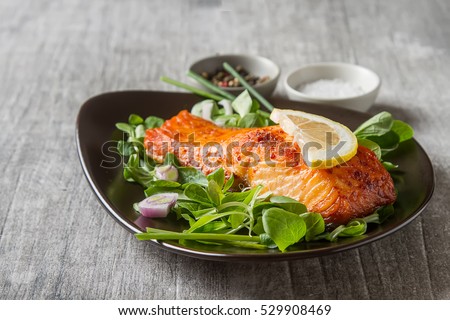 One piece of baked salmon grilled pepper lemon and salt on a brown plate with lettuce leaves. wood background