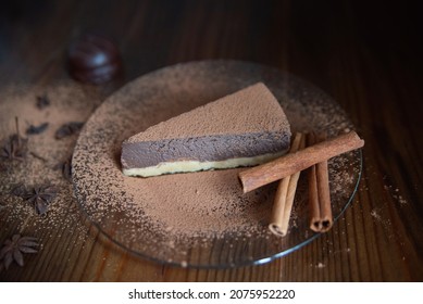 One Piece Of Chocolate Cheesecake On A Plate Decorated With Cinnamon, Candy And Cloves On A Wooden Background. Close-up