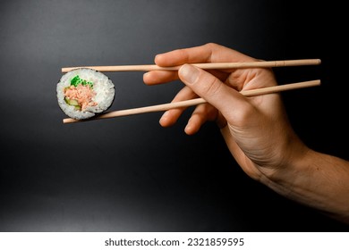 One piece of maki roll with tuna, cream cheese, avocado, cucumber and green calve hand holding with wooden chopsticks on black background. - Powered by Shutterstock