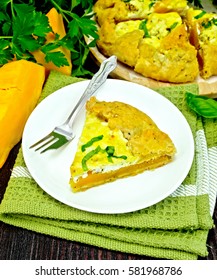 One piece of the pie of pumpkin, salty feta cheese, eggs, cream and herbs in a plate on towel, basil on a wooden boards background