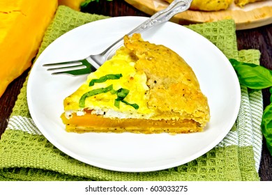 One piece of the pie of pumpkin, salty feta cheese, eggs, cream and herbs in a plate on a napkin, basil on a wooden boards background
