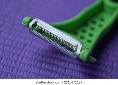 One Plastic Green Peeler With A Metal Blade With Teeth Lies On A Purple Table