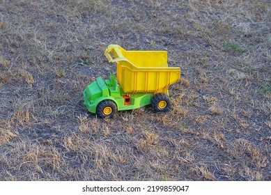 One Plastic Yellow Green Toy Car Truck Stands In Dry Grass On Gray Ground Outside