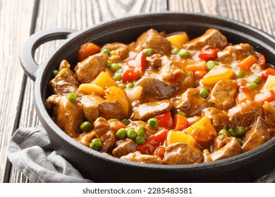 One pot of beef with potatoes, carrots, tomatoes, green peas, onions with spicy sauce close-up in a frying pan on a wooden table. Horizontal