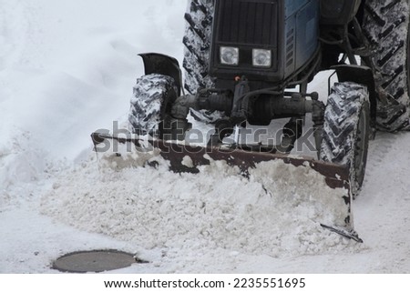 One powerful wheeled bulldozer tractor removes a snow with scraper shovel blade snowplow on city yard after heavy snowfall at winter day, top front view closeup