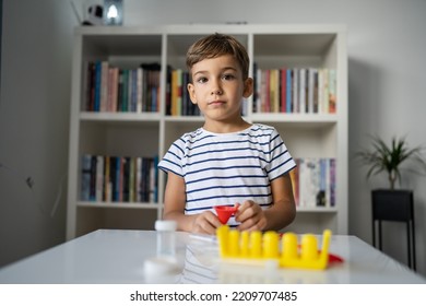 One Preschool Boy Playing At Home Sitting At The Table With Science Experiments Looking Straight At The Camera With Serious Face Childhood Growing Up Concept Copy Space Front View