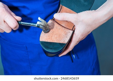 One Professional Shoemaker in Apron Repairing Sole of Black Polished Leather Mens Shoes With Hammer in Workshop. Horizontal Image Orientation - Powered by Shutterstock