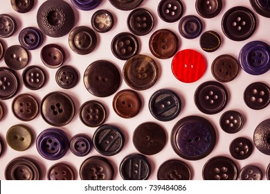 One red button on a background of dark vintage buttons for clothes. Bright individuality, dissimilarity, distinctive feature. View from above.