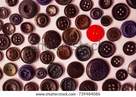 One red button on a background of dark vintage buttons for clothes. Bright individuality, dissimilarity, distinctive feature. View from above.