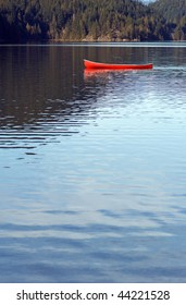 One Red Canoe Floats Empty On A Mountain Lake.