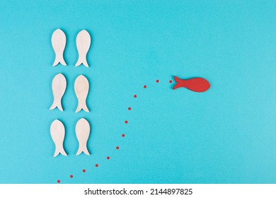 One red fish is swimming against the stream, opposite direction of the other fishes, being different, leadership and mindset concept 