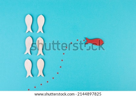 One red fish is swimming against the stream, opposite direction of the other fishes, being different, leadership and mindset concept 
