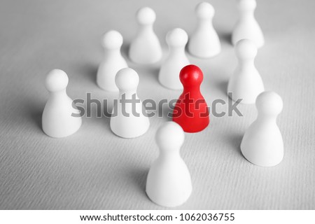 One red pawn among white ones on table. Difference and uniqueness concept