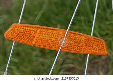 one red plastic reflector on the gray metal spokes of a bicycle wheel outdoors against a green background