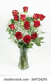 One red roses flower arrangement with its leaves and white babies breath blossoms in a clear glass vase. A dozen fresh cut red roses with babys breath in a glass vase