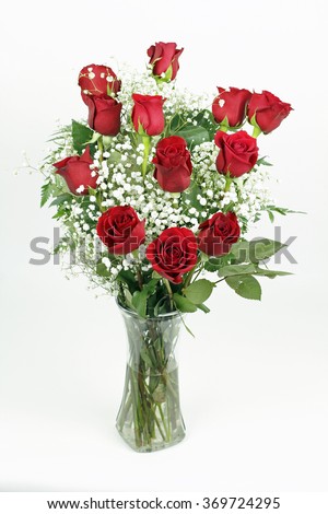 One red roses flower arrangement with its leaves and white babies breath blossoms in a clear glass vase. A dozen fresh cut red roses with babys breath in a glass vase