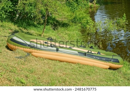 one rubber comfortable modern inflatable green boat for swimming and fishing stands on the green shore near the lake during the day